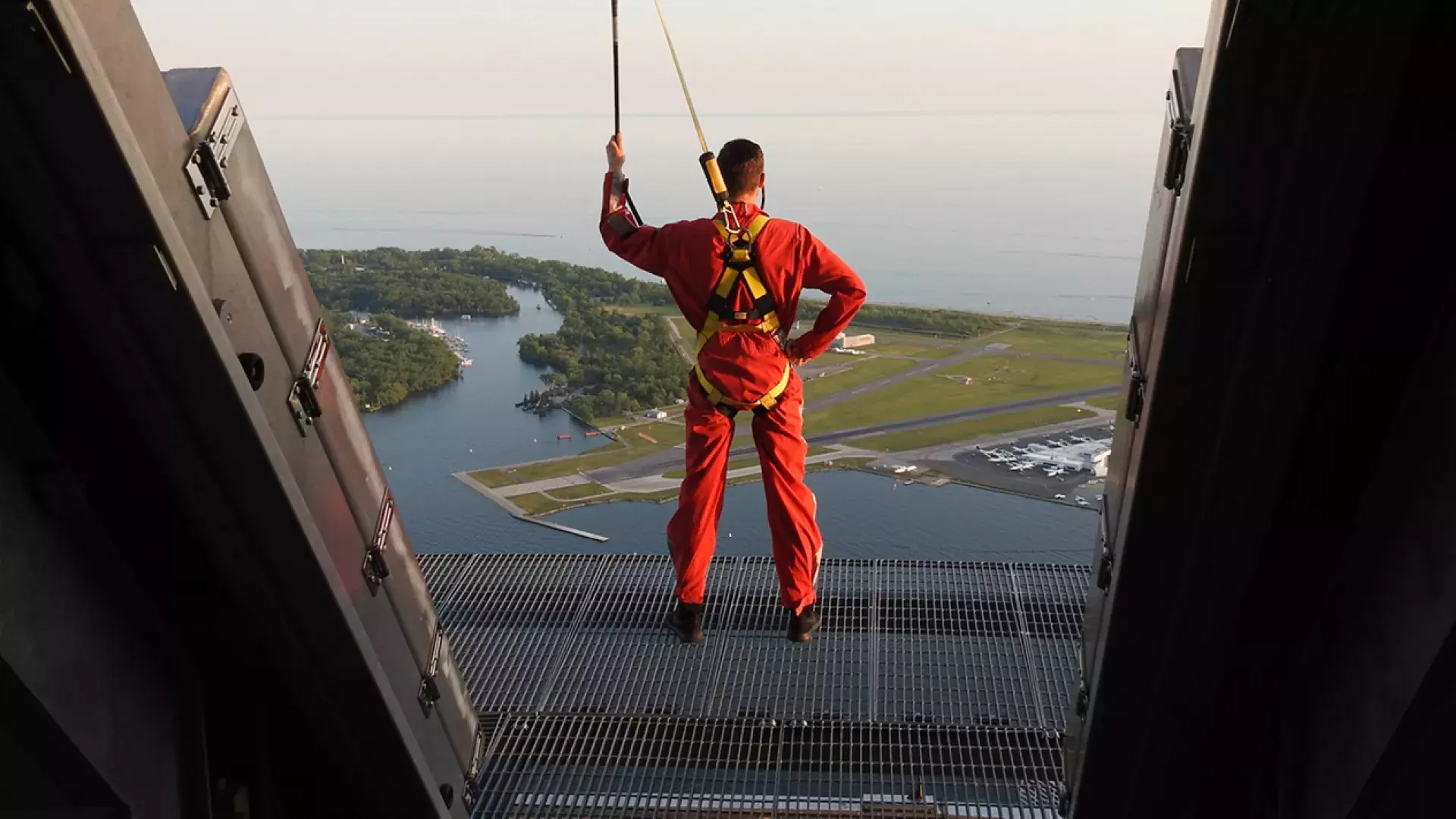 Person standing on the edge of of the Edgewalk wearing a harness and holding on to the security line