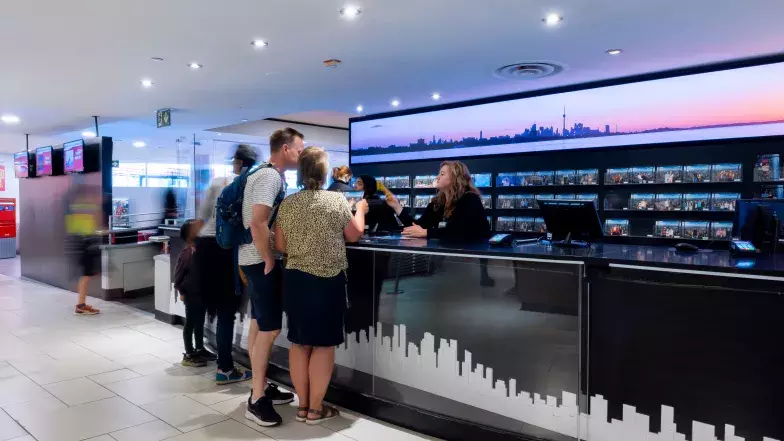 2 people looking at a brochure together while speaking with a person behind a counter