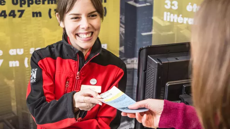 A CN Tower employee smiling while giving a ticket to a visitor