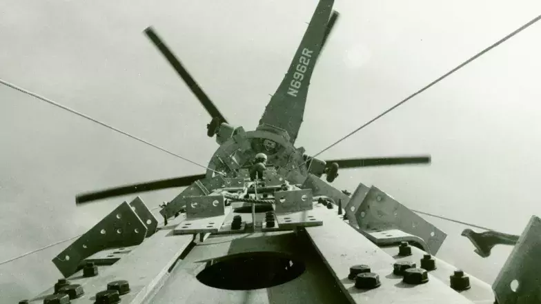 An older photo showing an helicopter above the tower. A person is at the top of the tower.