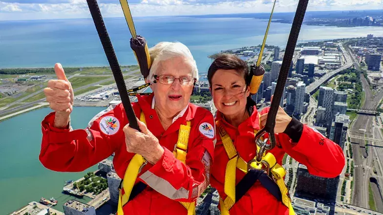 Two people with thumbs up and smiling with the city of Toronto far below on a bright but cloudy summer day