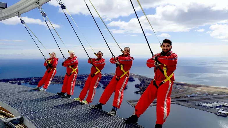 Group of five people with the backs leaning over the edge. Clouds and blue sky behind them.