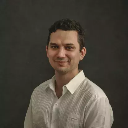 headshot of Alejandro Basulto, a Mexican man, wearing a white shirt smiling at the camera with a dark grey background.