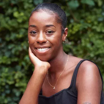 Artist Curtia Wright, a young black woman smiling at the camera wearing a black tank top with the trees as a background