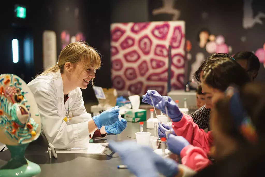 A woman in a lab coat guiding kids through a science experiment at the Montréal Science Centre.