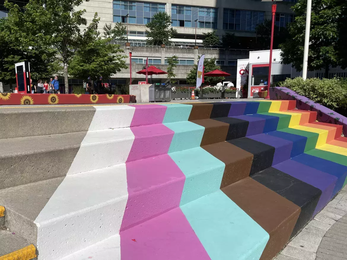 Rainbow art by Jo the Chalk Chick on stairs leading to the lower level of Canada Lands Square. We see more colourful art in the background with sunflowers.