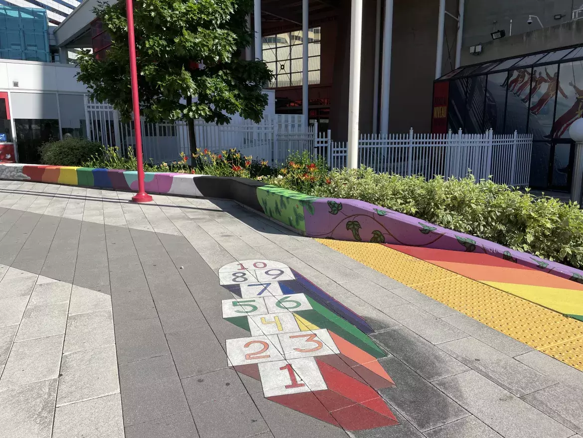 Colourful hopscotch painting on Canada Lands Square. In the background, more paintings of plants and rainbows. 