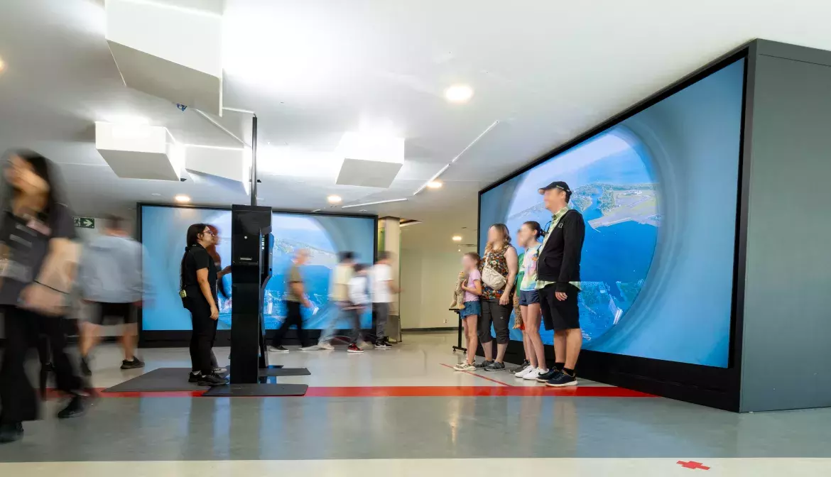 A family gets their picture taken in front of a large screen displaying content.