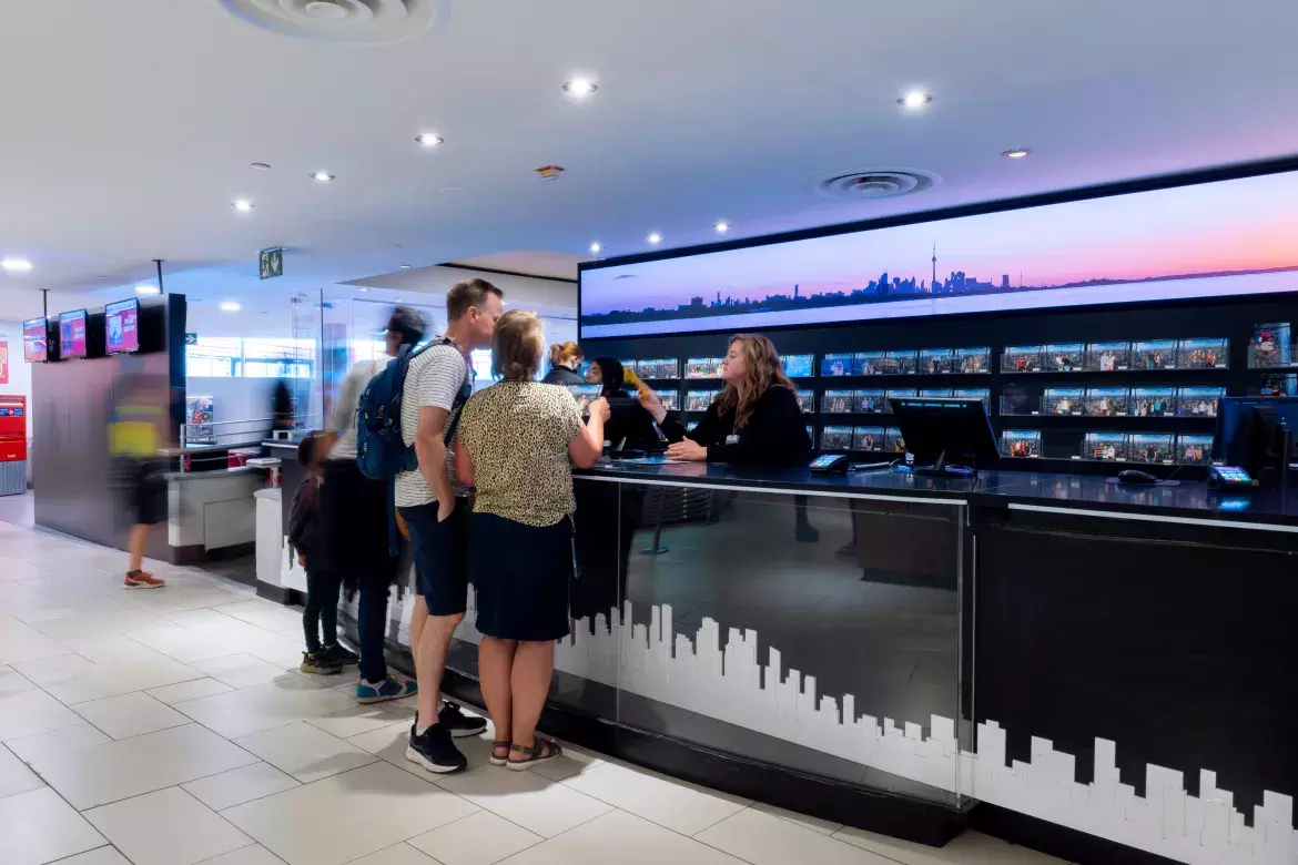 2 people looking at a brochure together while speaking with a person behind a counter