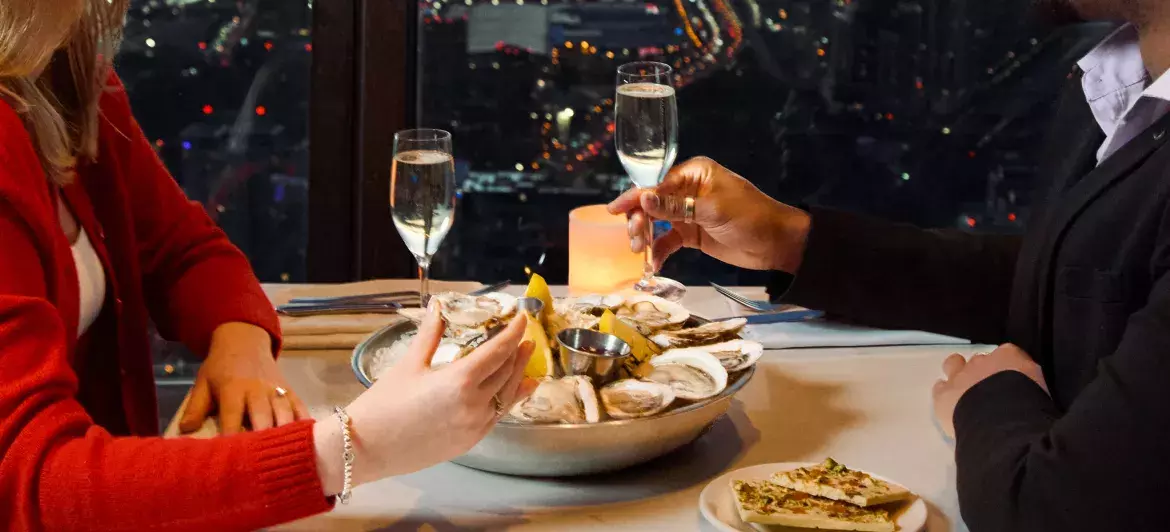 A couple enjoying fresh oysters, chocolate and champagne together at 360 Restaurant. In the background, we can see the view of Toronto at night through the windows.