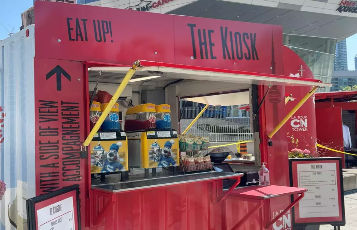 An outdoor Food and Beverage Red Kiosk located in Canada Lands Square with various products like slushies and chips displayed.